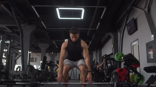 Attractive man of athletic build trains in gym doing squats with barbell, front view. Male bodybuild