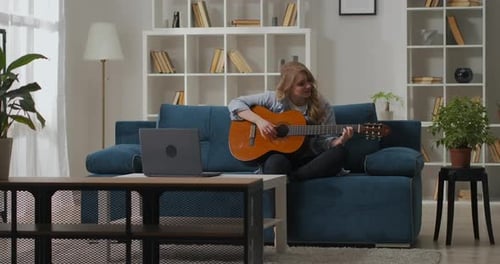 Woman Plays Guitar on Couch at Home