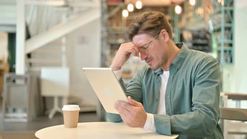 Disappointed Middle Aged Man Reacting To Loss on Tablet in Cafe