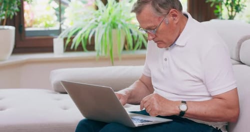 Senior Man Using Laptop Computer Indoors on Couch