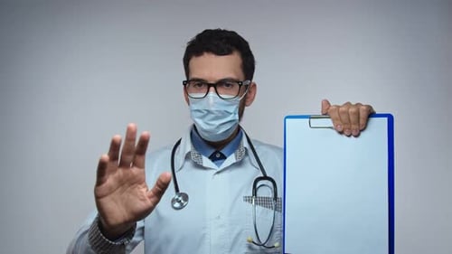 The Doctor in a Mask Holds a Form with Space for Text and Shakes His Head Negatively
