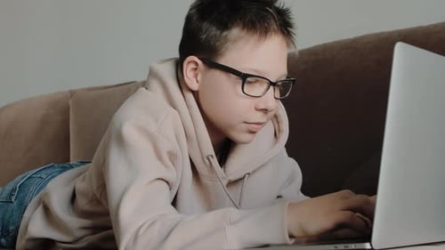 Focused Teen Typing on Laptop While Lying Down