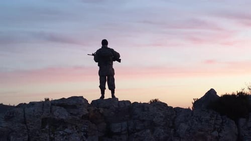 Silhouetted Soldier with Rifle on Mountain Top at Twilight