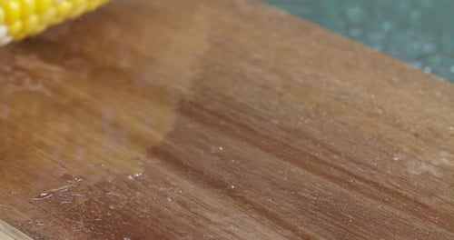 Slow motion close up of a fresh, ripe corn on the cob rolling along a wood cutting board