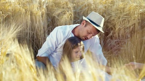Happy family with little daughter having picnic in wheat field in summer