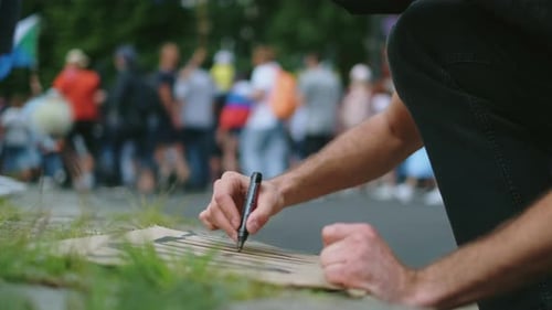 Man Writes on Sign at an Outdoor Protest