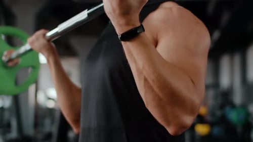 Closeup of torso sporty man training in gym, lifting barbell with hands, front view.