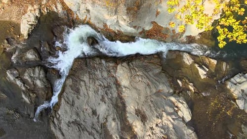 Top down aerial view of small mountain stream with fast moving clear water between rocky