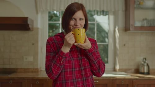 Woman Drinking From Mug in Kitchen Smiling