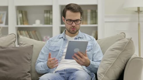 Man Sitting On Couch Using Tablet With Frustration