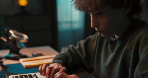 Teen Types on Laptop at Desk at Night