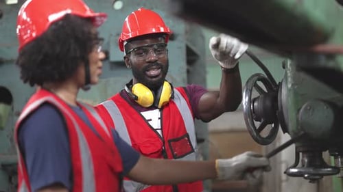 Afroamerikaner männlicher Fabrikarbeiter, der große Maschine mit Kollegen bedient