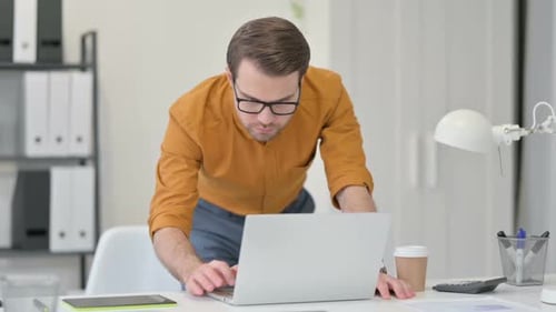 Young Man Standing Working on Laptop in Office
