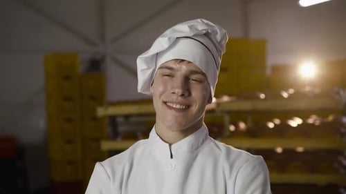 Portrait of Young Baker in Uniform Looking with Smile at Camera in a Bakery