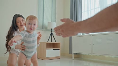 Caucasian baby boy child learn to walk with parents support in house.
