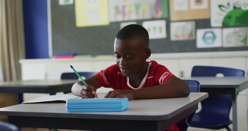 Boy at Desk Writing, Smiling in Classroom