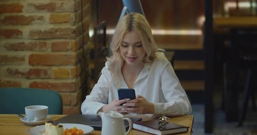 Young Woman Using Mobile Phone in a Cafe Drinking Tea