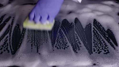 Gloved Hand Cleaning Foamy Surface with Sponge