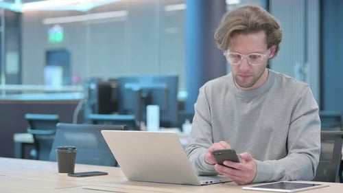 Young Adult Works With Laptop and Smartphone