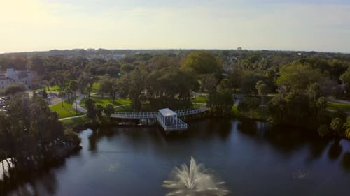 Flug über einen Springbrunnen in einem Teich und in Richtung eines Parks mit Bäumen bei Sonnenuntergang