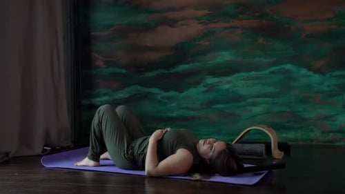 a Woman in a Green Jumpsuit is Lying on a Sports Mat