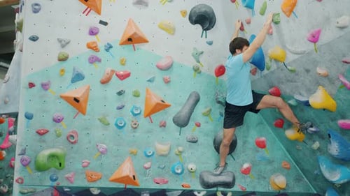 Strong Guy in Sports Outfit Climbing Up Colorful Artificial Wall in Gym Gripping Rocks