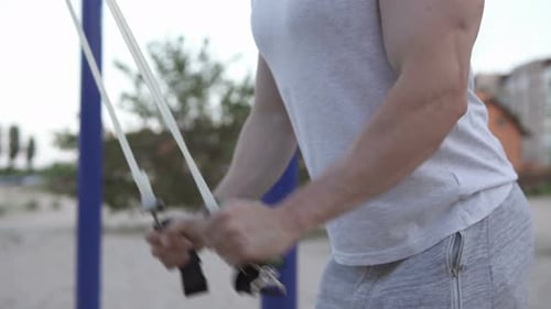 The athlete performs exercises with the help of an expander on the street in quarantine.