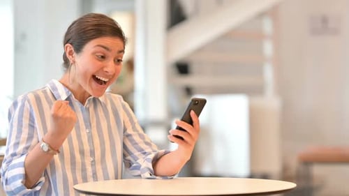 Woman Celebrating with Smartphone Indoors