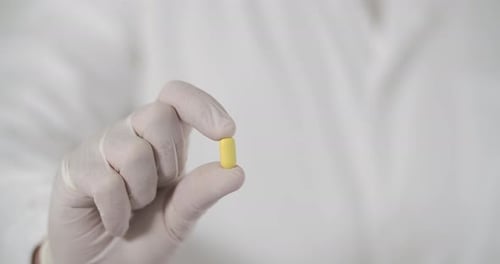 Hand with Gloves Holding a Yellow Pill