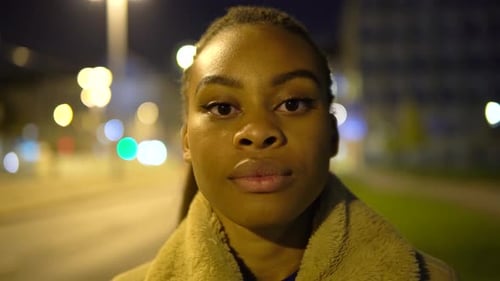 A Young Black Woman Looks Seriously at the Camera in a Street in an Urban Area at Night Closeup