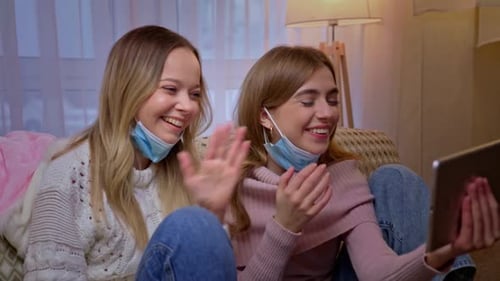 Pretty Young Women in Medical Protective Masks Sitting on Couch in Living Room and Talking Webcam on