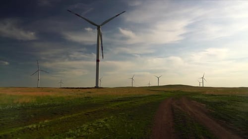 Bewegen Sie die Blätter einer großen Windkraftanlage in einem Feld vor dem Hintergrund eines wolkenblauen Himmels in der Nähe