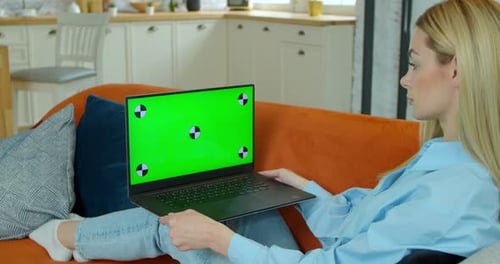 Pretty Girl Making Video Call on Laptop. Woman at Home Uses Green Mock-up Screen Laptop. She's
