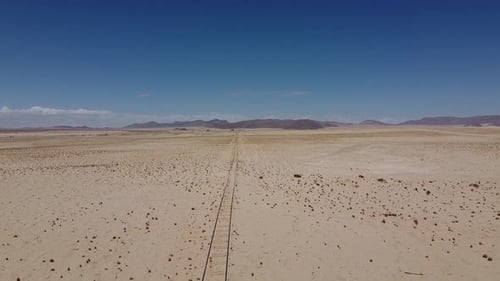 Chemin de fer couvert de sable à travers le désert, montagnes lointaines et ciel bleu
