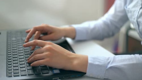Manos femeninas escribiendo en un teclado portátil en una oficina blanca