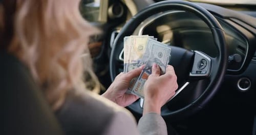 Female Hands Behind Steering wheel in Luxury Car Counting Cash Financial Profits in the Parked Car.