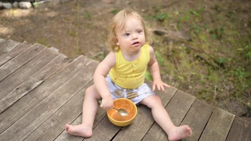 Kleines lustiges süßes blondes Mädchen Kind Kleinkind mit schmutziger Kleidung und Gesicht isst Babynahrung Obst oder