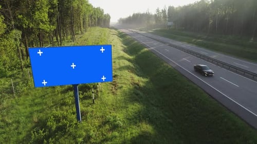 Billboard poster with blue screen and tracking markers on a highway.