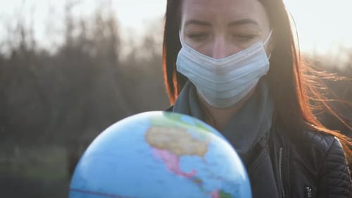 Woman with Mask Looks at Globe of Earth