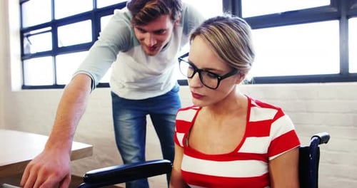 Woman in Wheelchair Working with Colleague in Office
