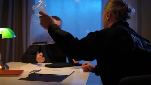 Back View Police Officer Showing Evidence Weapon in Plastic Package to Suspect Blurred Man Sitting