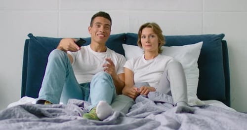 Young Mixed Couple Is Watchning TV in Bedroom, Woman Is Bored