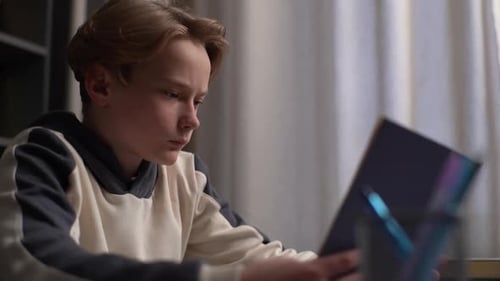 Side Closeup View of Smart Serious Pupil Boy Reading School Paper Book Sitting Alone at Desk in
