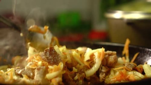 Frying pan with meat and vegetables close-up. Female rka mixes contents.