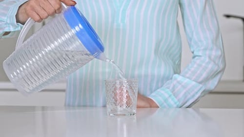 Woman Pours Refreshing Water into Glass in Kitchen