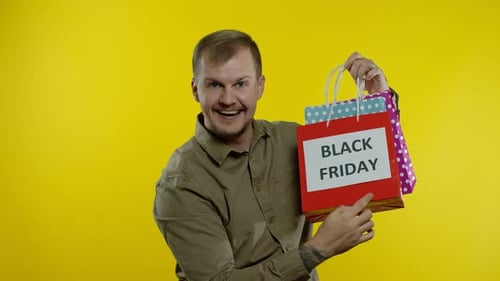 Man Showing Black Friday Inscription on Shopping Bags, Smiling, Satisfied with Low Prices Purchases