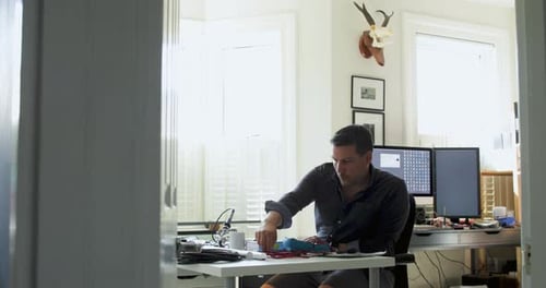 Man Soldering Wires at Desk with Electronics
