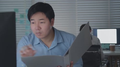 Man Reviews Documents at Computer in Office