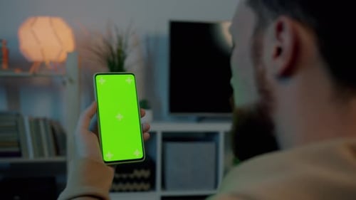 Closeup of Male Hand Holding Chroma Key Green Screen Smartphone While Man Watching Content on