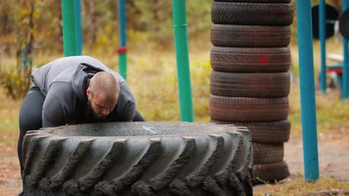 A Big Man Bodybuilder Turning Over the Tire on the Ground - Training Outdoors